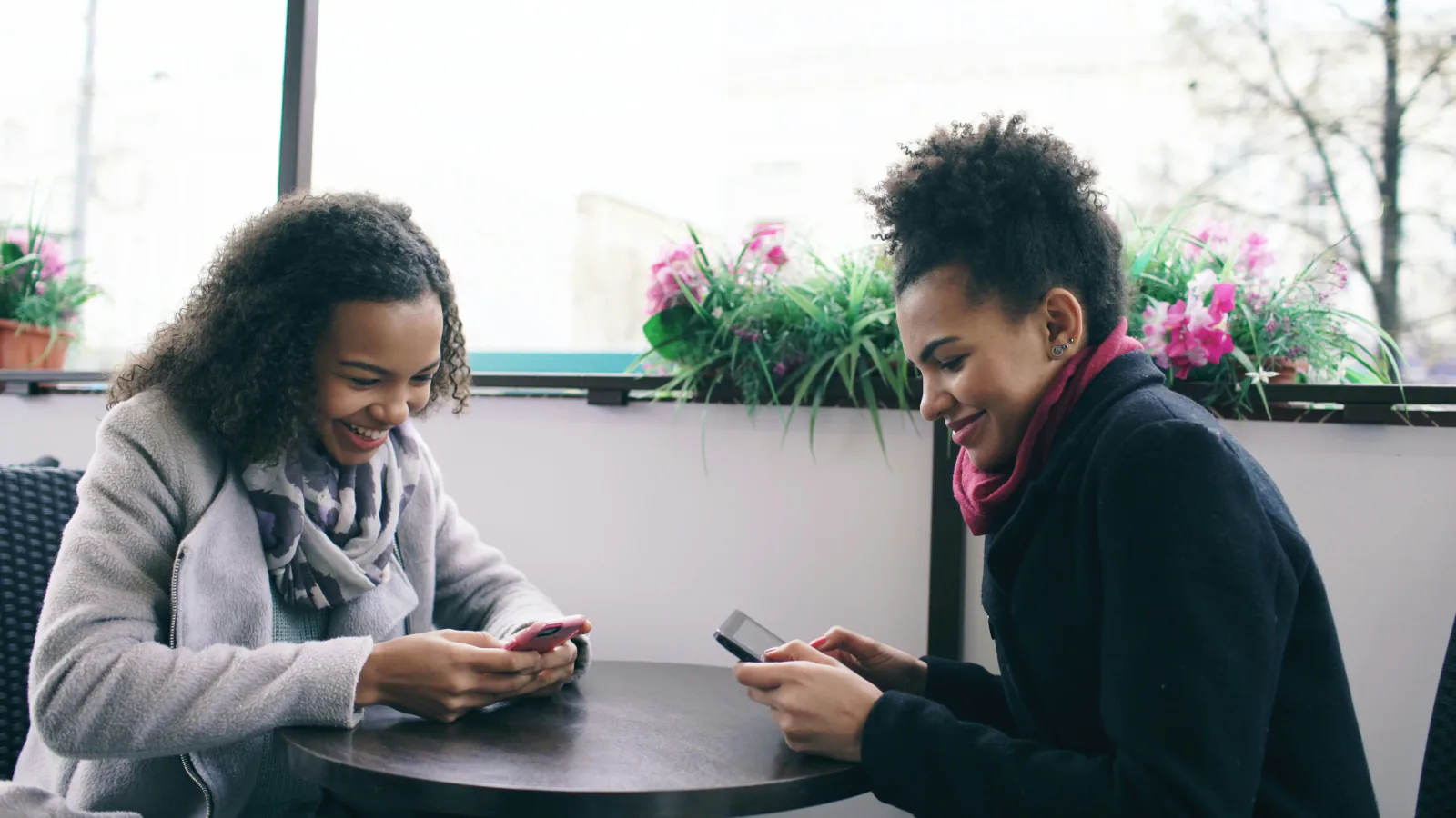 Two friends looking at phones at a cafe table