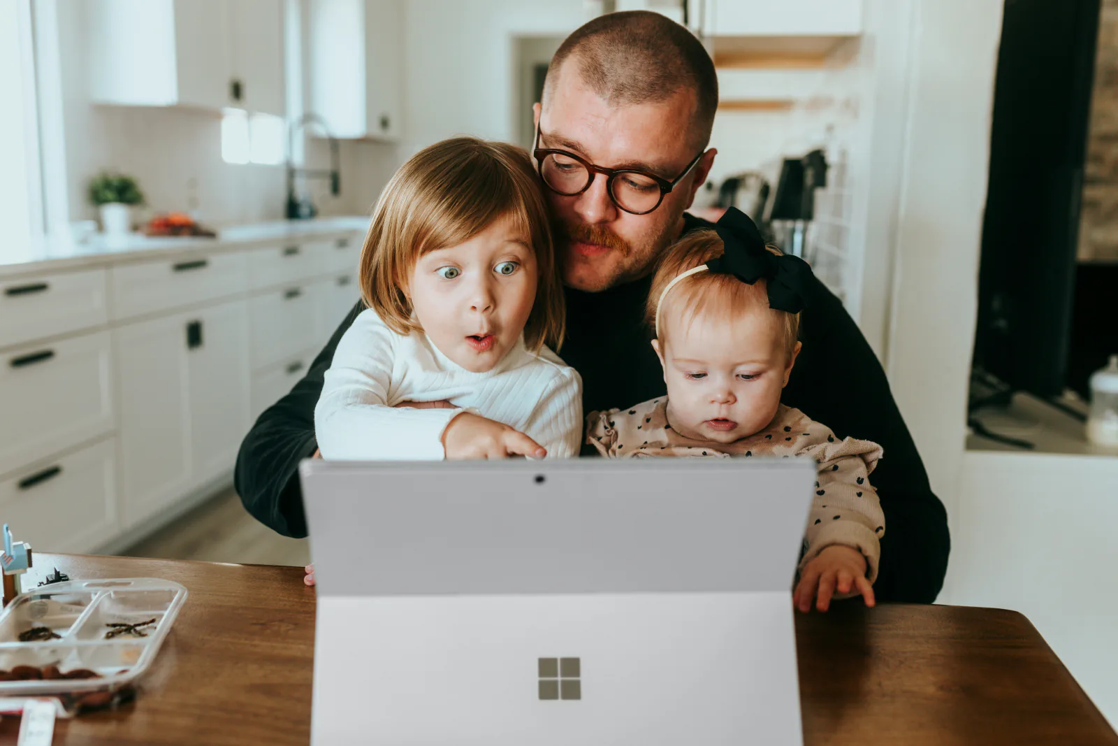 A parent and two children looking at a laptop in a kitchen