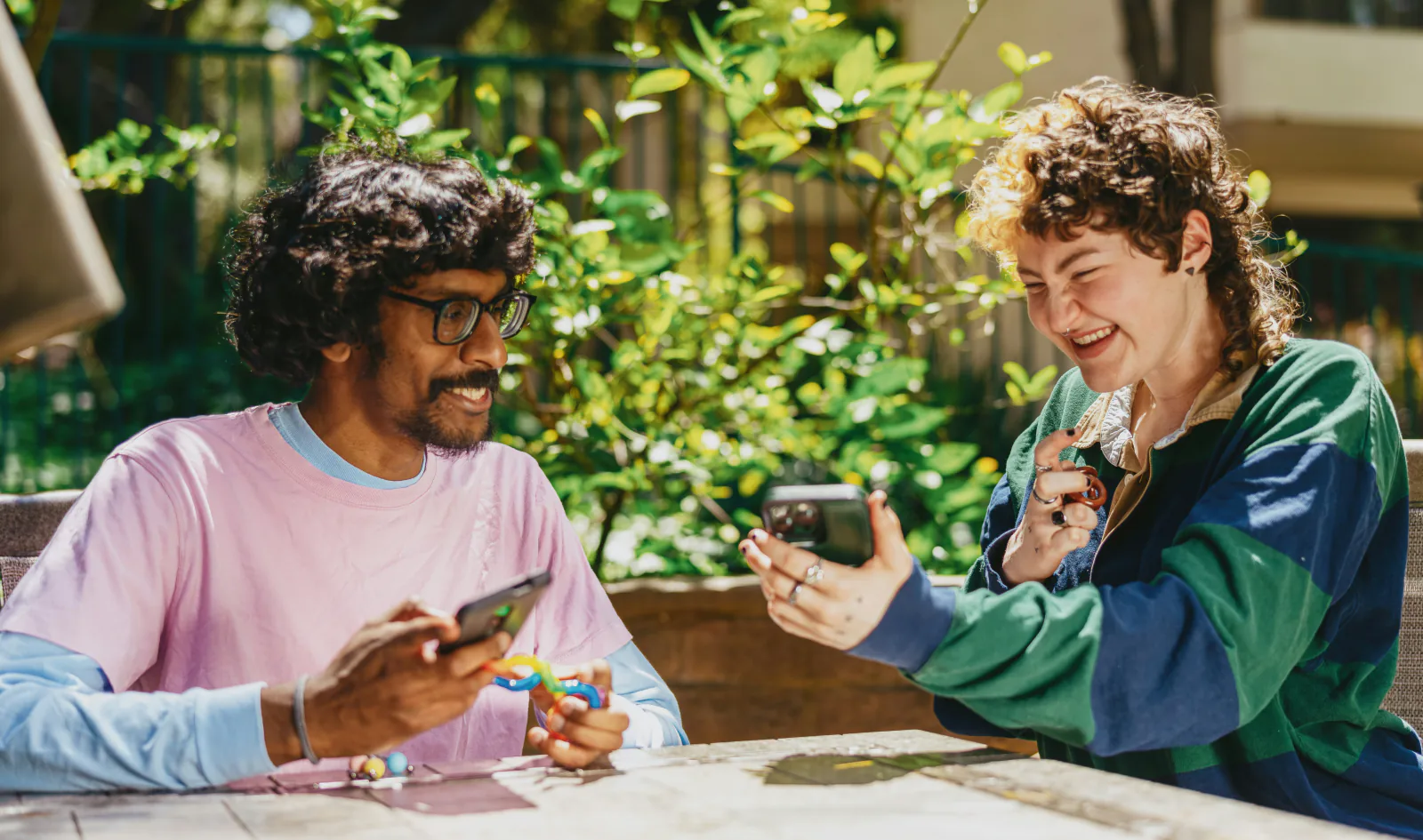 Two friends laughing while looking at their phones outdoors